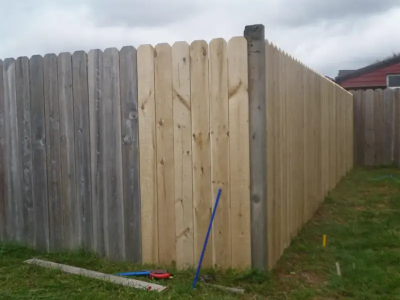 Timber fence with new palings beside older weathered palings after a repair